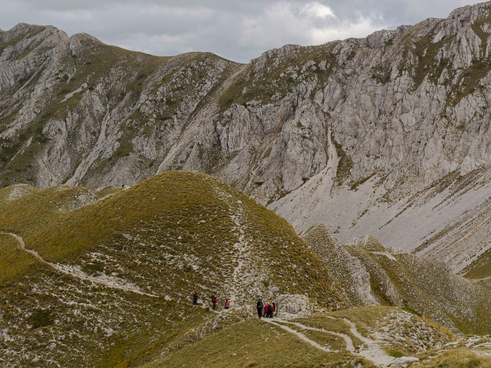 Escursionisti sul sentiero verso il lago di Pilato tra praterie d'alta quota e rocce calcaree Escursionisti sul sentiero verso il lago di Pilato tra praterie d'alta quota e rocce calcaree