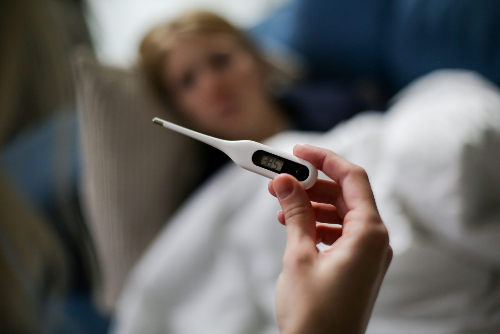 Persona a letto con termometro in bocca, sintomi febbre influenza in inverno