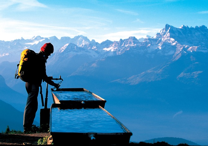 Brunnen Hiker at a rest stop at a fountain high above Leysin in the region of les Diablerets, Canton of Vaud. In the background the massif of Dents du Midi, 3178 m high. Swiss_Image_sts0433